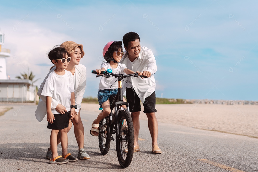 Família passeando pela praia ensinando filho a andar de bicicleta