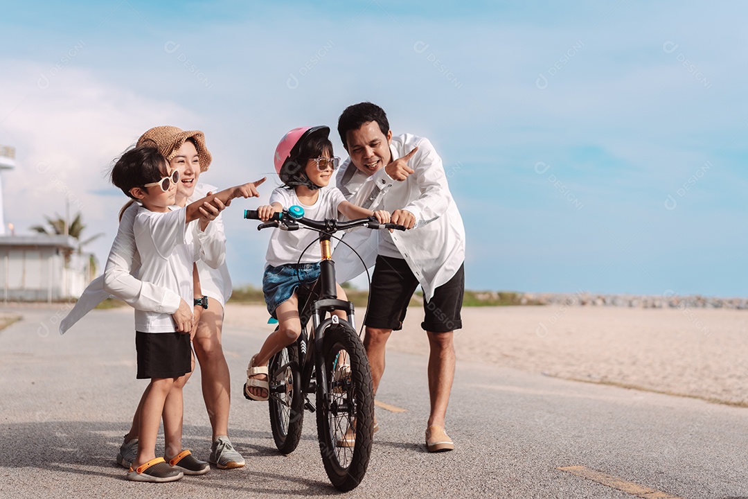 Família passeando pela praia ensinando filho a andar de bicicleta