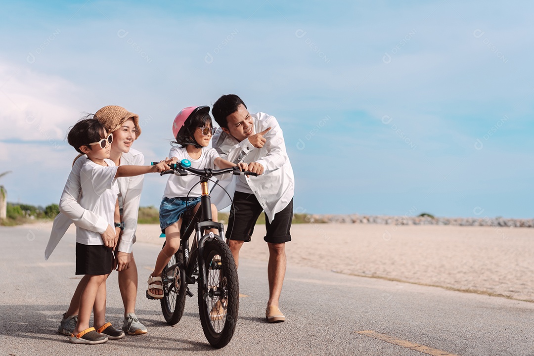 Família passeando pela praia ensinando filho a andar de bicicleta