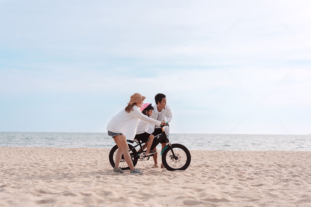 Família passeando pela praia ensinando filho a andar de bicicleta