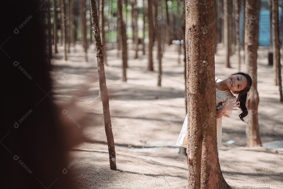 Menina brincando se escondendo atrás da árvore e acenando com a família