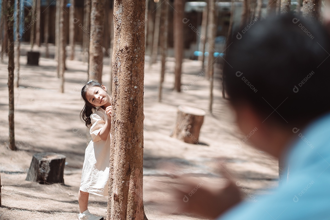 Menina brincando se escondendo atrás da árvore e acenando com a família