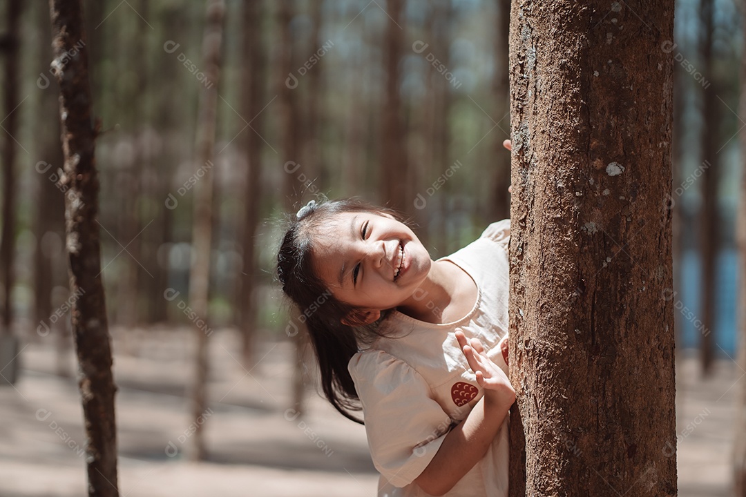 Menina brincando se escondendo atrás da árvore e acenando com a família
