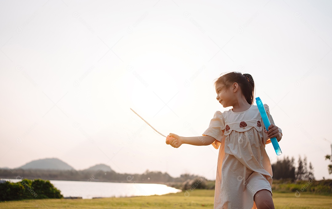 Menina jogando bolhas de sabão no parque ao pôr do sol