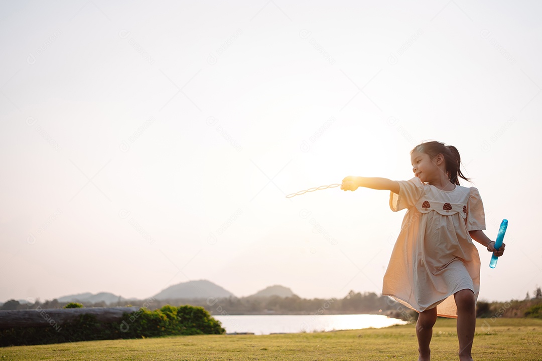 Menina jogando bolhas de sabão no parque ao pôr do sol