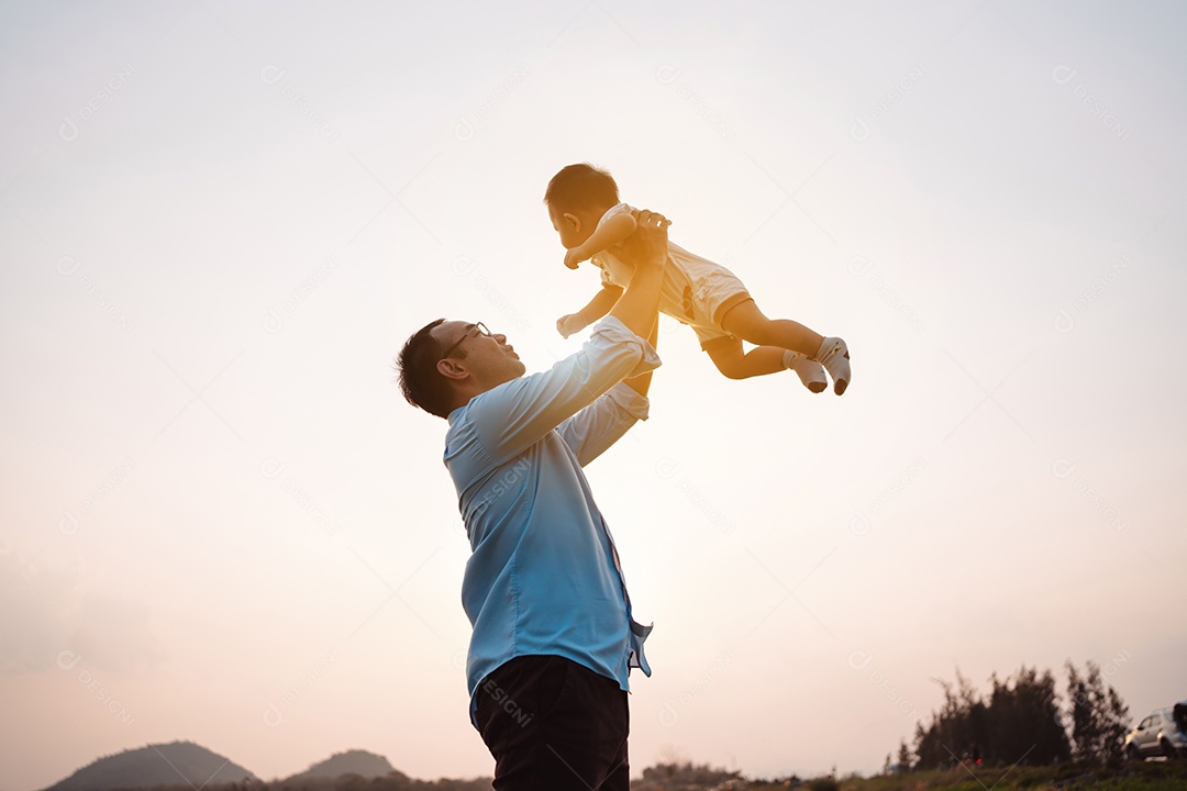 Paternidade levantando filho bebê desfrutando no parque perto do rio ao pôr do sol.
