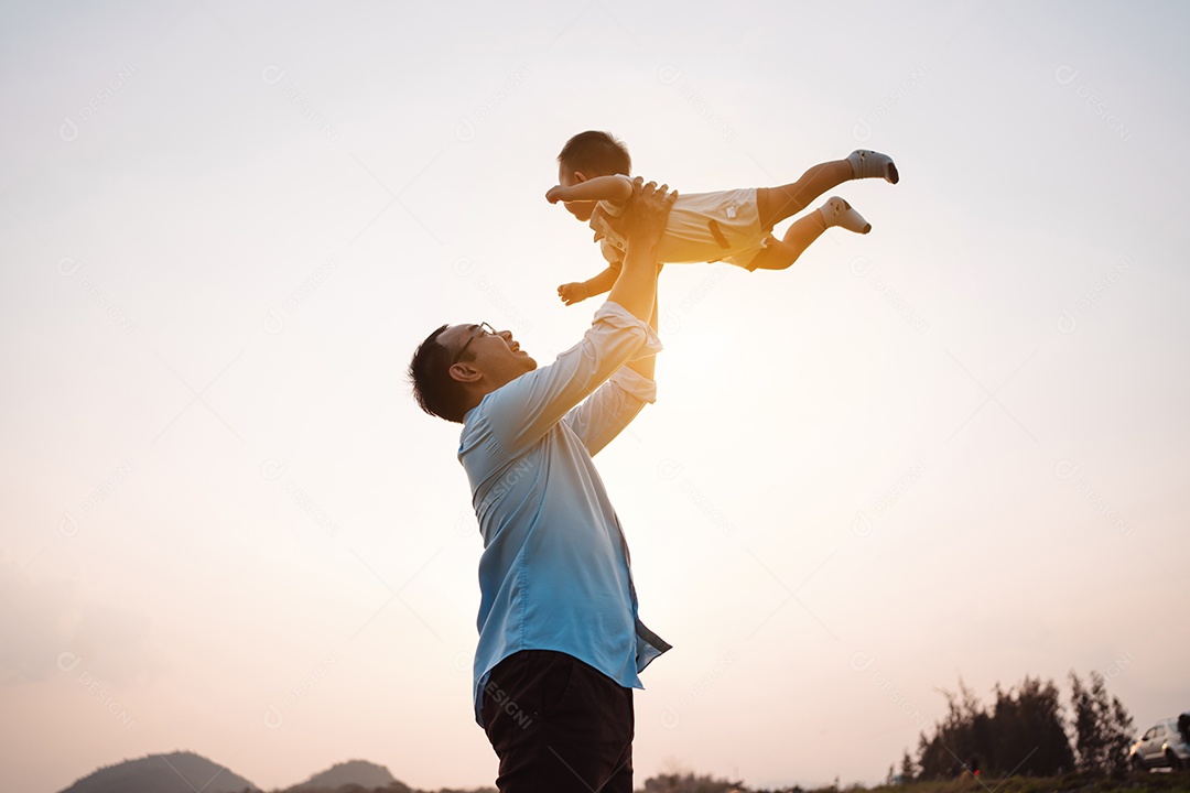 Paternidade levantando filho bebê desfrutando no parque perto do rio ao pôr do sol.