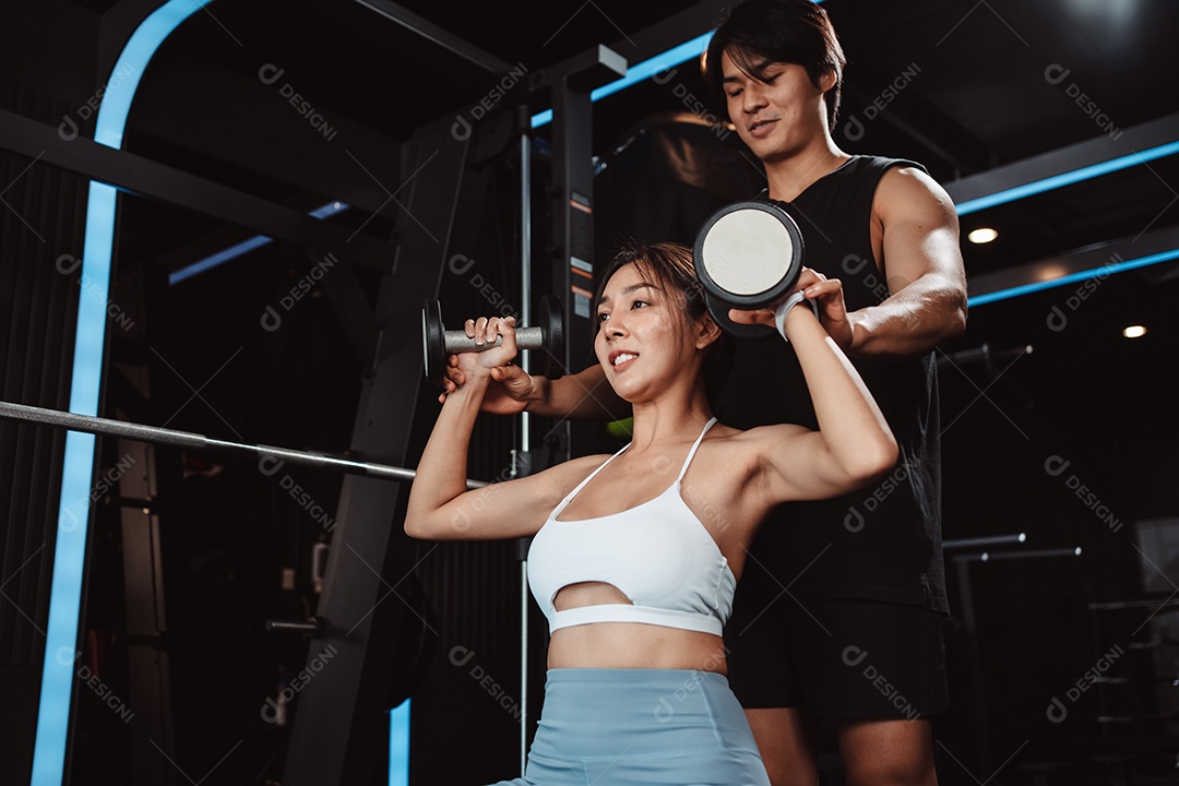 Mulher malhando fisiculturista com assistência de treinamento para suportar pesos na academia.