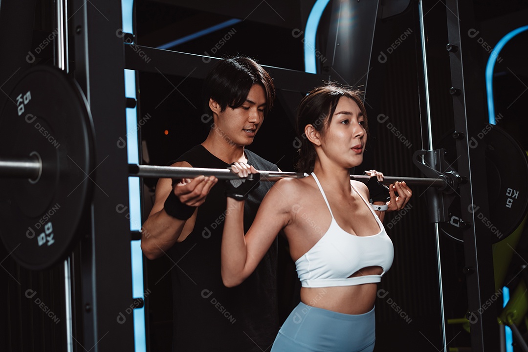 Mulher malhando fisiculturista com assistência de treinamento para suportar pesos na academia.