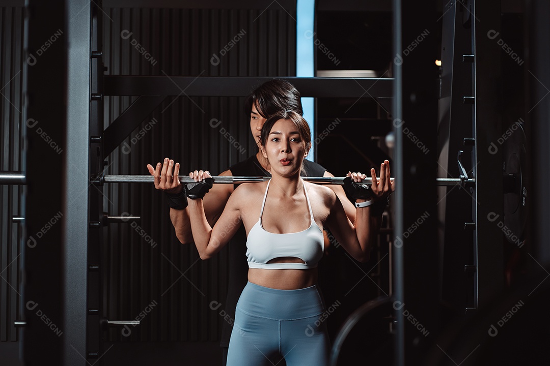 Mulher malhando fisiculturista com assistência de treinamento para suportar pesos na academia.
