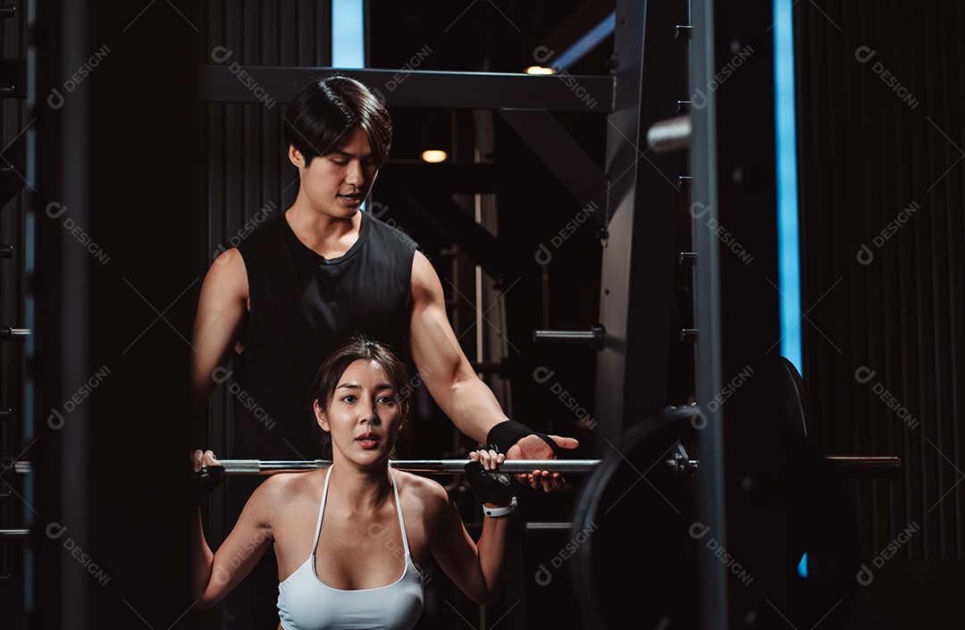 Mulher malhando fisiculturista com assistência de treinamento para suportar pesos na academia.
