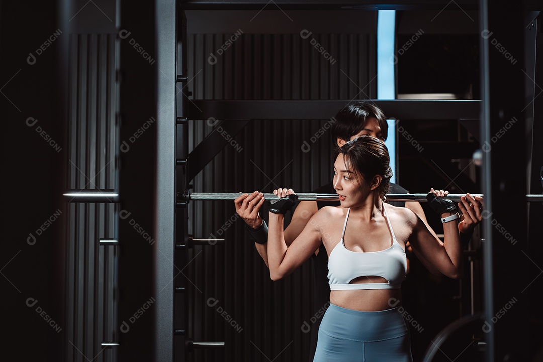 Mulher malhando fisiculturista com assistência de treinamento para suportar pesos na academia.