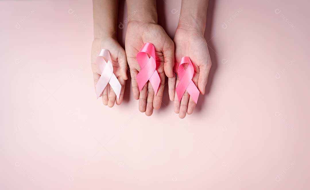Mãos de pessoas segurando fitas rosa em fundo rosa, conscientização sobre o câncer de mama, dia mundial do câncer