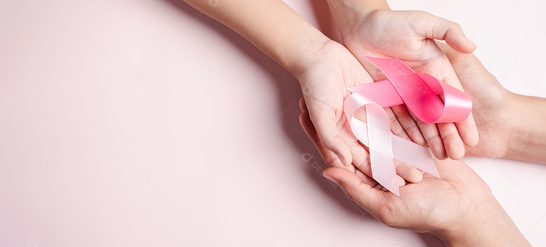Mão segurando a fita rosa que está entre fitas coloridas em fundo rosa, conscientização do câncer, dia mundial do câncer