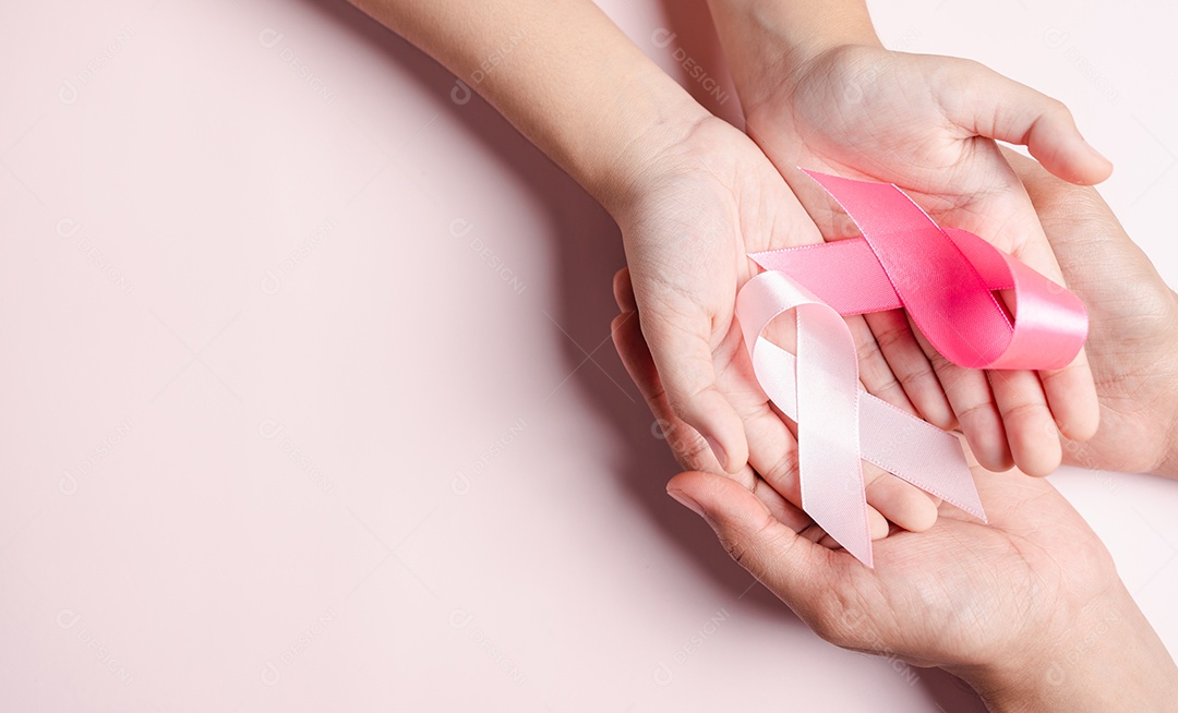 Mãos de pessoas segurando fitas rosa em fundo rosa, conscientização sobre o câncer de mama