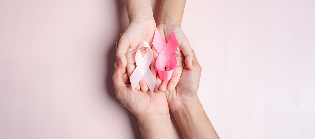 Mãos de pessoas segurando fitas rosa em fundo rosa, conscientização sobre o câncer de mama