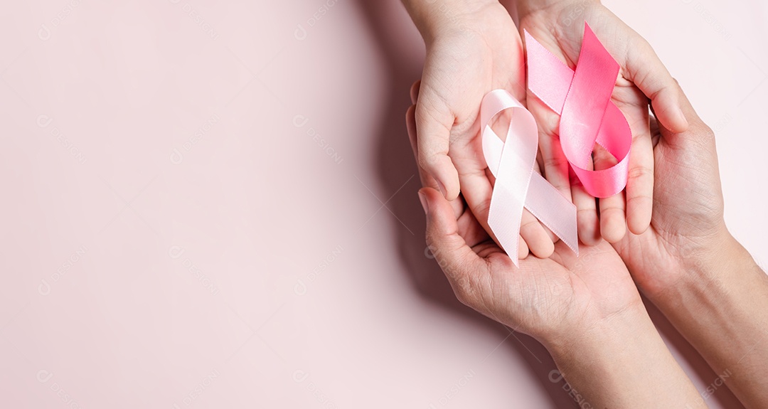 Mãos de pessoas segurando fitas rosa em fundo rosa, conscientização sobre o câncer de mama