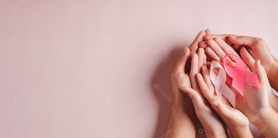 Mãos de pessoas segurando fitas rosa em fundo rosa, conscientização sobre o câncer de mama