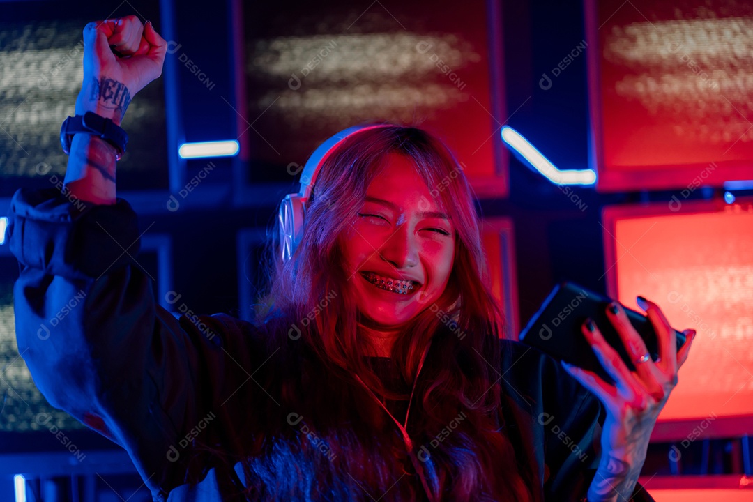 Jogador asiático jogando videogame online ganhando entusiasmo no PC com efeito de iluminação, transmissão ao vivo em casa.