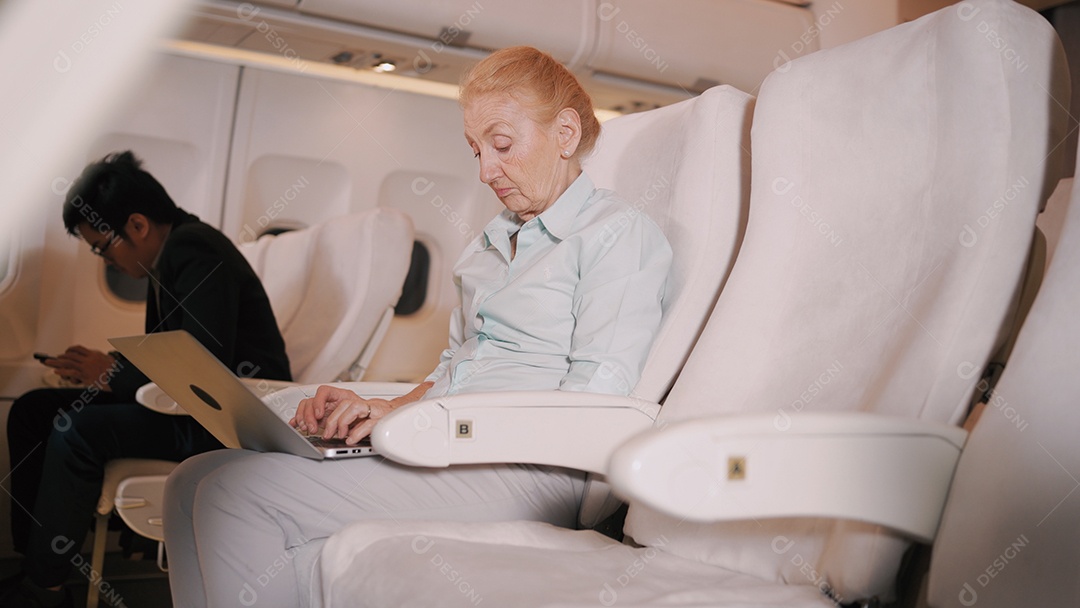 Empresária idosa trabalhando com laptop digital no voo de avião