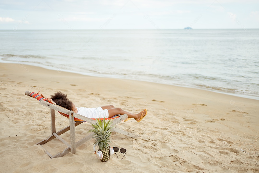 Criança americana africana jogando sentada na cadeira da praia