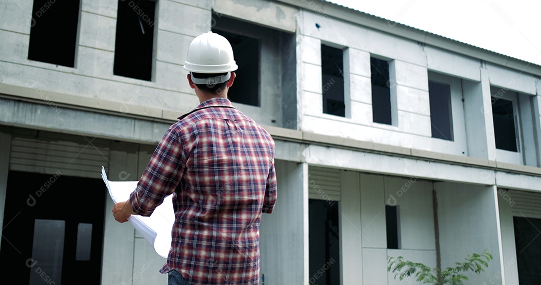 Homem de negócios jovem asiático no capacete segurando a planta e olhando para longe em pé dentro de casa.