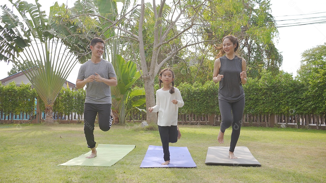 Feliz família asiática brincando com crianças fazendo exercícios de ioga na grama do parque durante o dia.