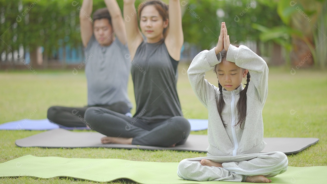 Feliz família asiática brincando com crianças fazendo exercícios de ioga na grama do parque durante o dia.