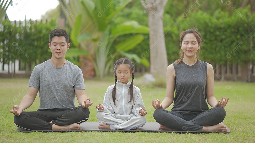Feliz família asiática brincando com crianças fazendo exercícios de ioga na grama do parque durante o dia.