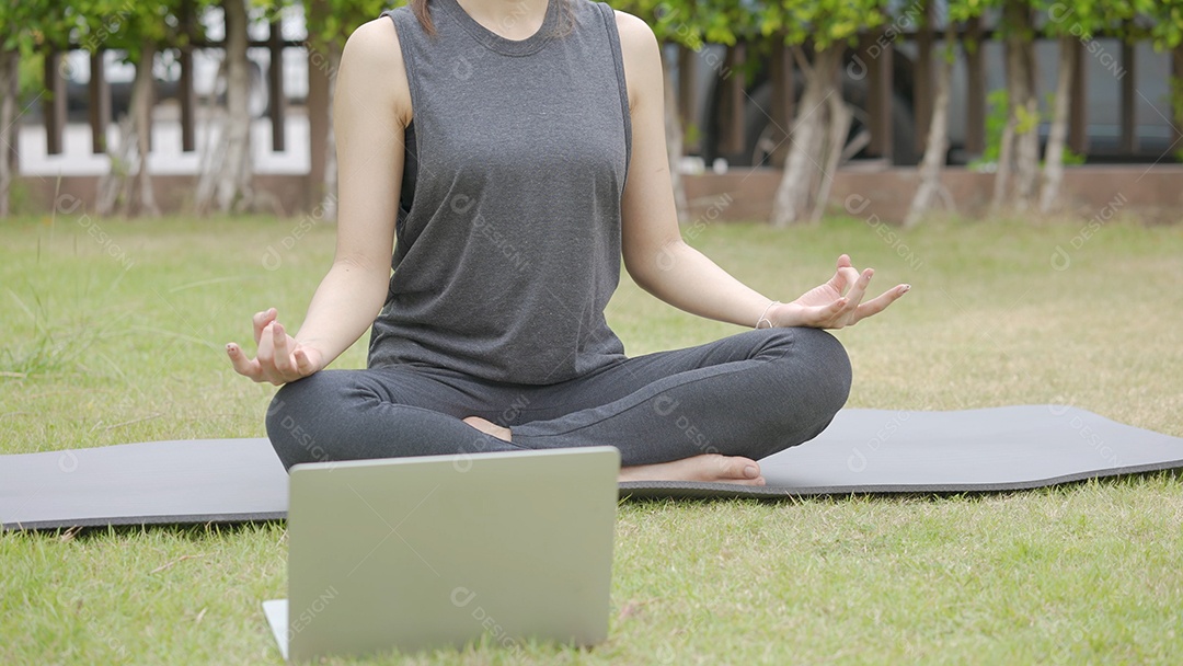 Feliz jovem asiática praticando aula de ioga online no jardim ao ar livre durante a quarentena.