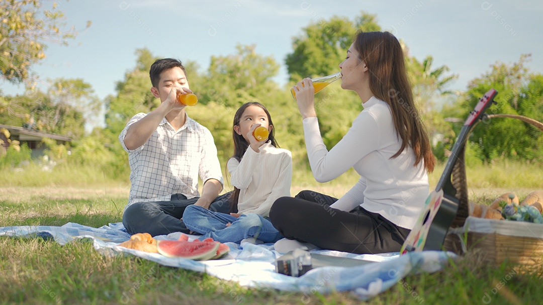 A família feliz asiática e a garotinha estão bebendo suco de laranja