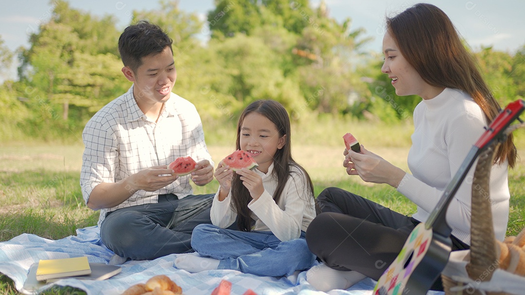 A família feliz asiática e a garotinha estão comendo melancia e se divertiram juntos durante o piquenique