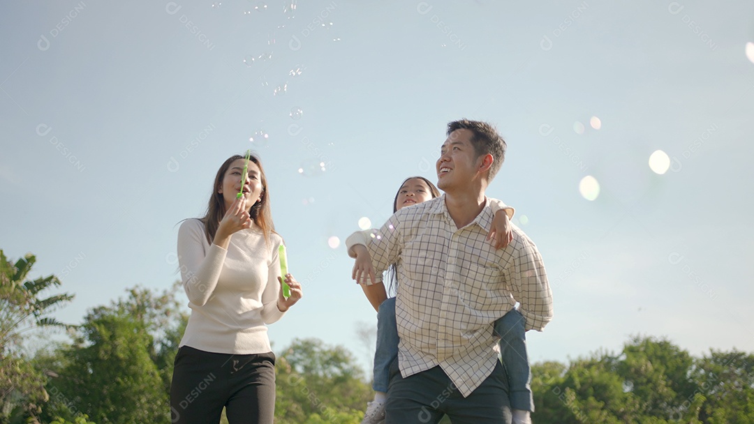Feliz jovem pai asiático pegando carona com sua filhinha enquanto a mãe corre para brincar com ela no parque
