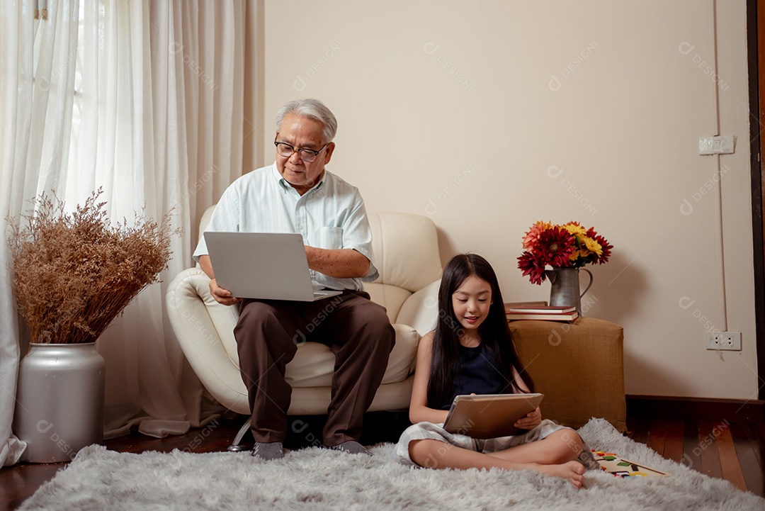 O vovô bonito asiático está segurando um livro enquanto sua neta está desenhando em um papel