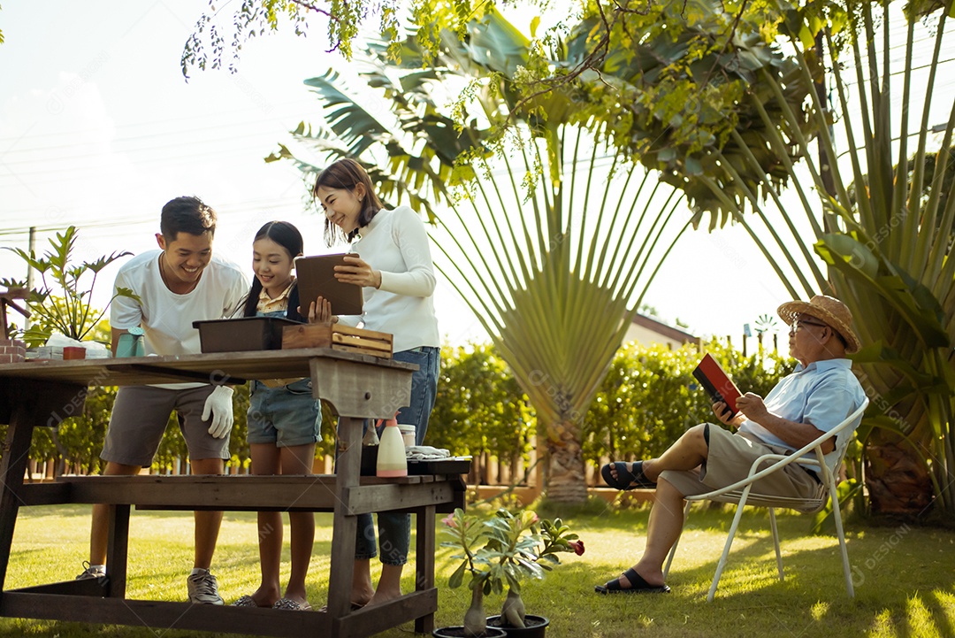 Casal asiático com filha jardinando enquanto assiste laptop juntos no jardim do quintal.