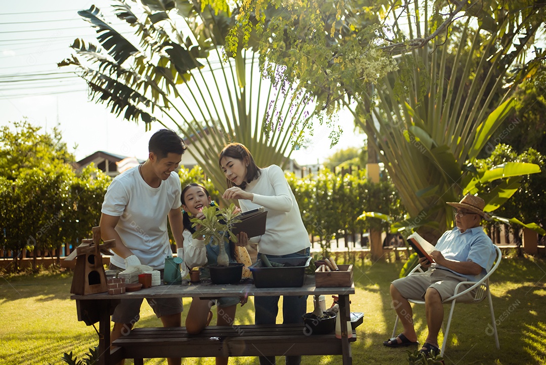 Casal asiático com filha jardinando enquanto assiste laptop juntos no jardim do quintal.