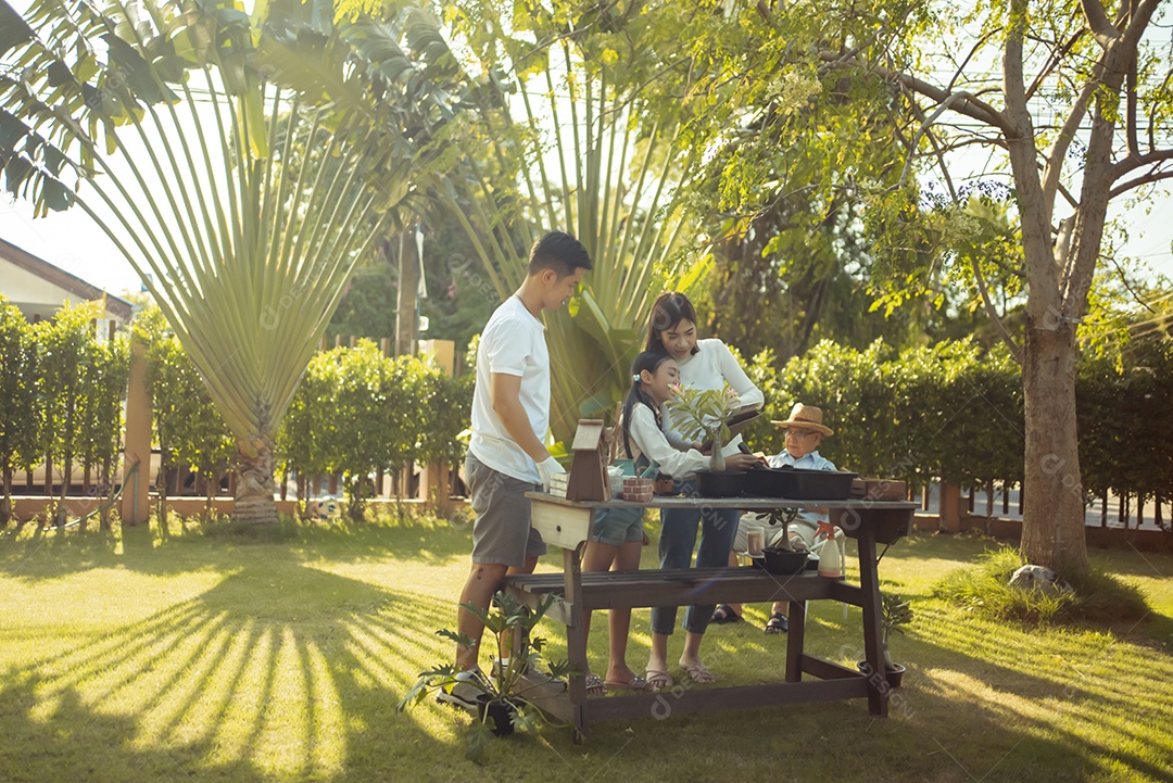 Casal asiático com filha jardinando enquanto assiste laptop juntos no jardim do quintal.