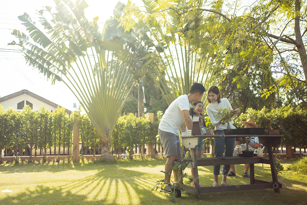 Casal asiático com filha jardinando enquanto assiste laptop juntos no jardim do quintal.