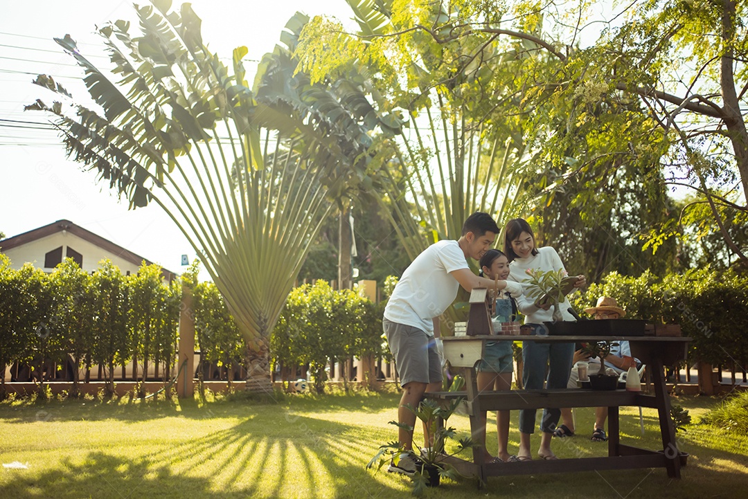 Casal asiático com filha jardinando enquanto assiste laptop juntos no jardim do quintal.