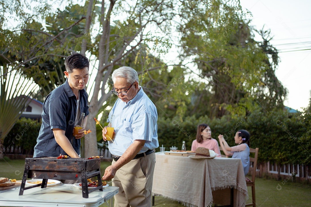 Família asiática feliz jantando e saboreando suco em copos em jantar de churrasco