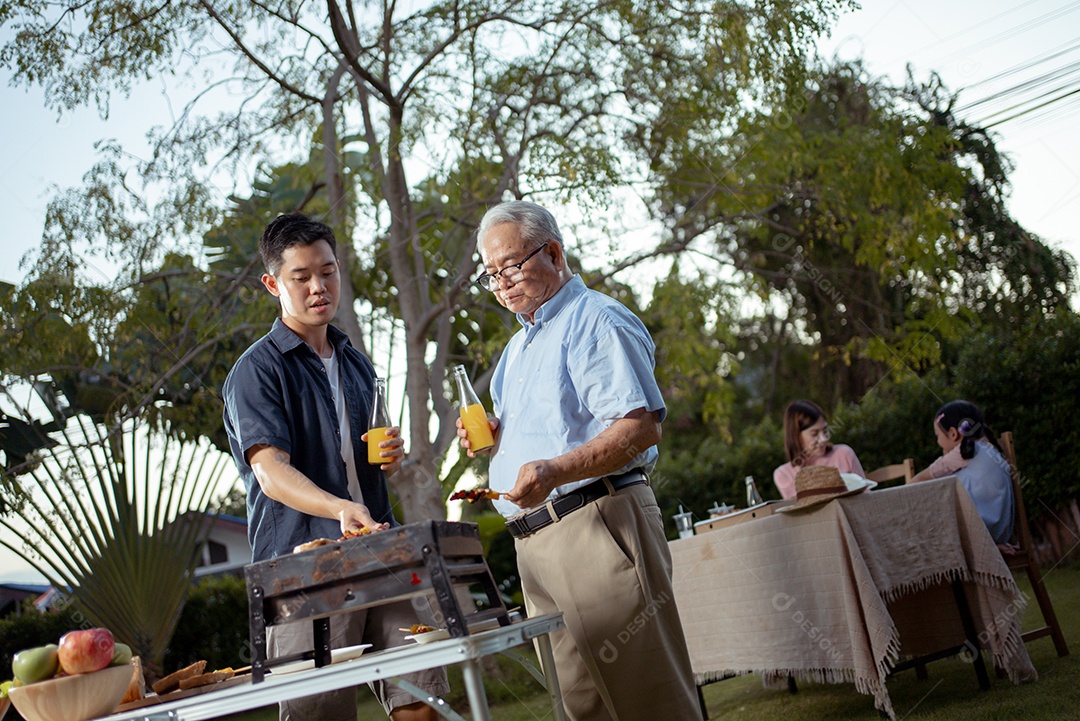 Família asiática feliz jantando e saboreando suco em copos em jantar de churrasco