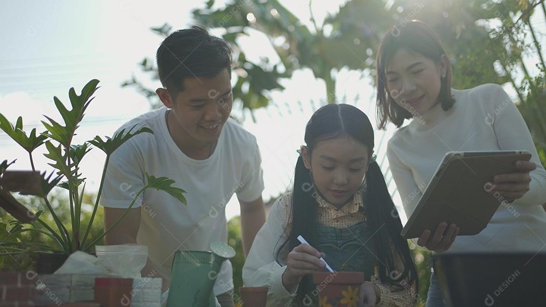 Casal asiático com filha jardinando enquanto assiste laptop juntos no jardim do quintal.