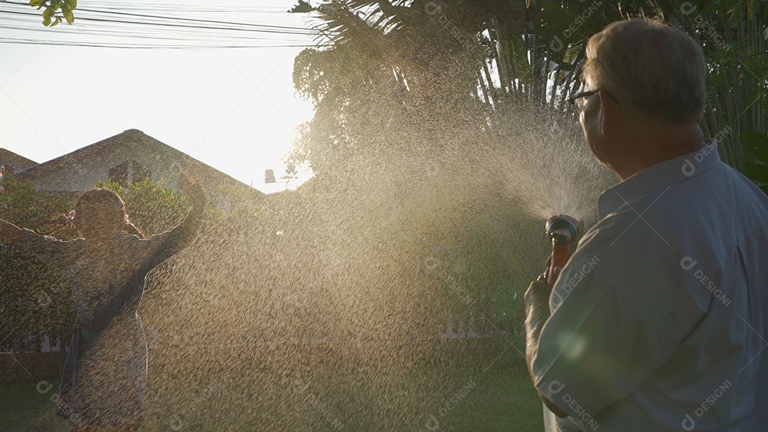 Feliz vovô sênior asiático derramando água de uma mangueira.