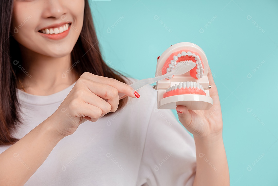 O sorriso bonito dental da jovem mulher asiática ensina a escovação correta dos dentes