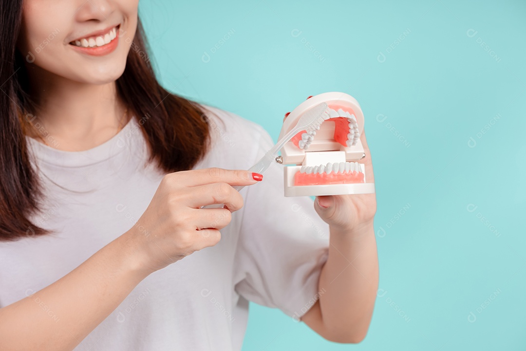 O sorriso bonito dental da jovem mulher asiática ensina a escovação correta dos dentes