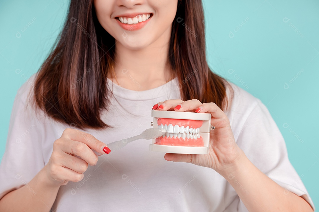 O sorriso bonito dental da jovem mulher asiática ensina a escovação correta dos dentes