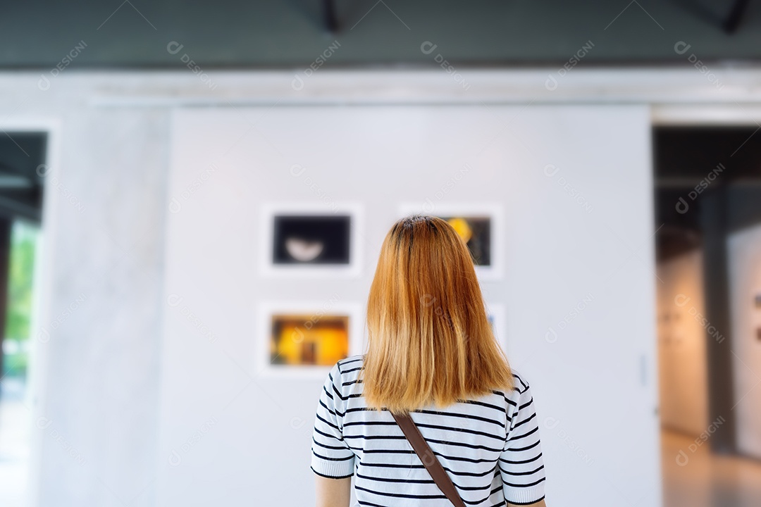 Mulher visitando a galeria de arte suas fotos olhando na parede, observando quadro