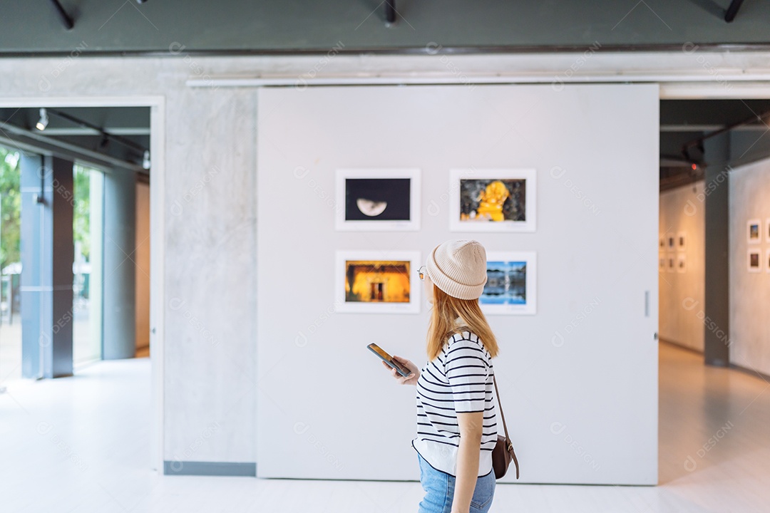 Mulher visitando a galeria de arte suas fotos olhando na parede, observando quadro