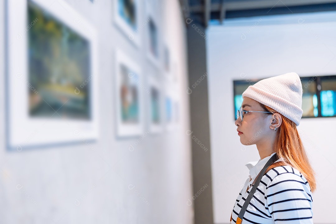 Mulher visitando a galeria de arte suas fotos olhando na parede, observando quadro