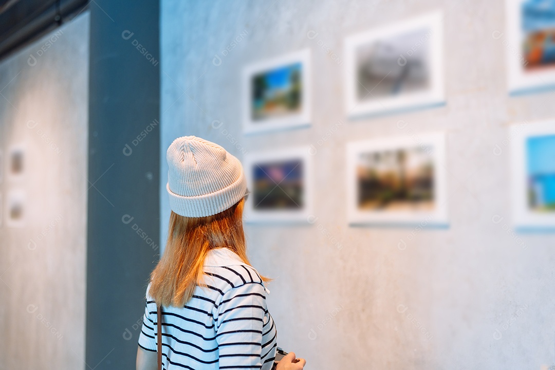 Mulher visitando a galeria de arte suas fotos olhando na parede, observando quadro